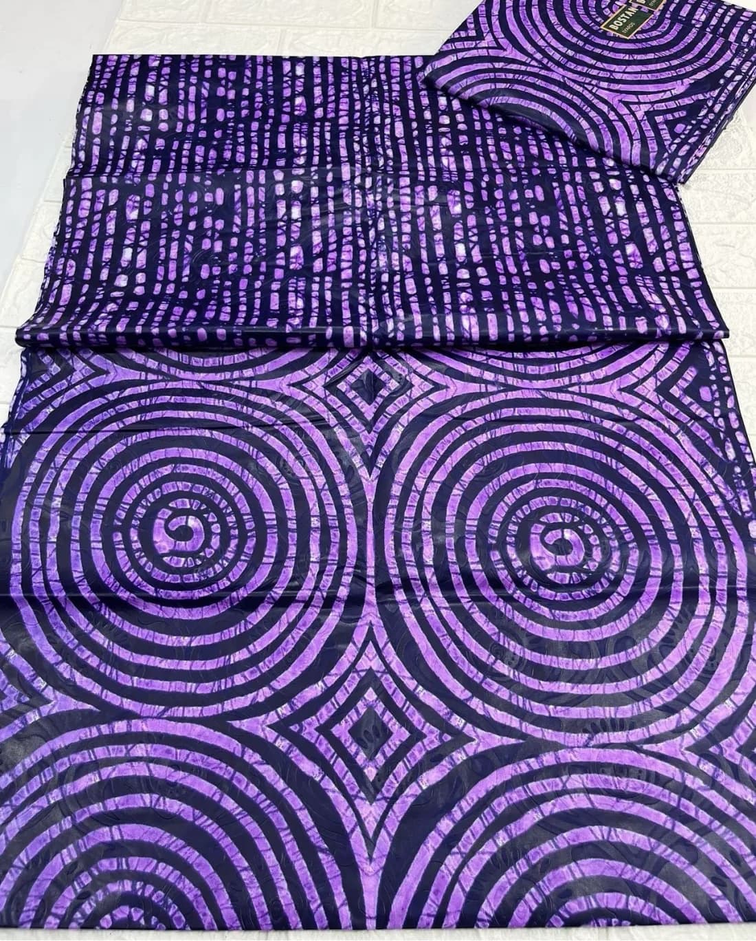 Folded Adire cloth in purple and deep indigo, with large spirals and broken stripes