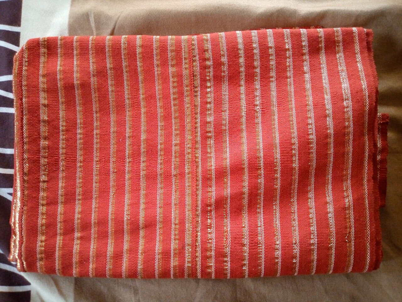 Folded red Alaari Aso Oke with fine gold and white stripes