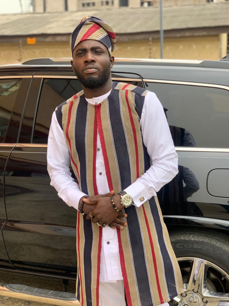 Man wearing a long navy, beige and red striped Aso Oke waistcoat and matching fila